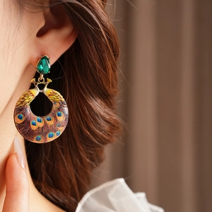 Detailed close-up of a vintage peacock enamel crescent earring on a model