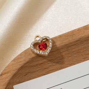Macro detail of a heart-shaped gold pendant with a red gemstone and white crystals