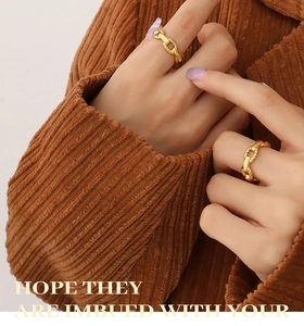 Detail view of two gold chain rings worn on finger against brown corduroy background
