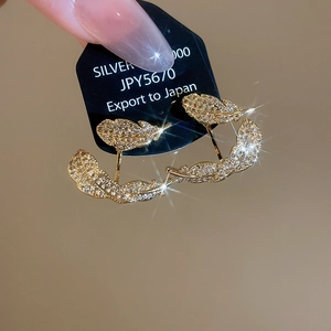 Macro detail of gold-plated leaf earrings with cubic zirconia on black export card