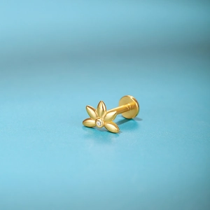 Macro detail of gold flower piercing stud with center diamond on blue texture background