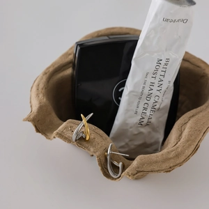 Detail of two-tone gold and silver steel stud earrings displayed on a paper bowl edge
