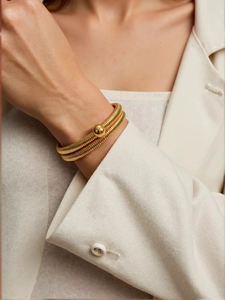 Detail of 18k gold spiral double-layer bracelet with a polished metal bead on a wrist