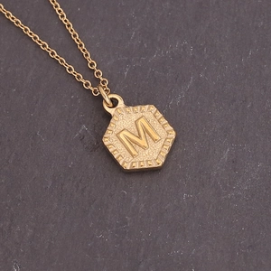 Macro shot of gold-plated hexagon pendant featuring the letter M with radiant texture