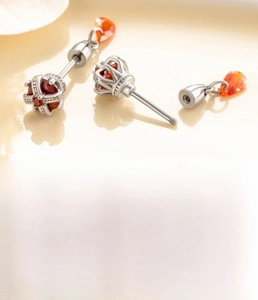 Macro detail of silver crown cartilage stud with orange-red zircon and screw back closure