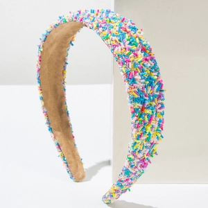 Close-up of wide headband featuring colorful candy sprinkles decoration on a white stand