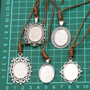 Detail of five antique silver alloy pendant bases with brown PU cords on a green cutting mat