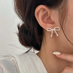 Close-up of silver bow stud earrings with intricate beaded texture worn by a model