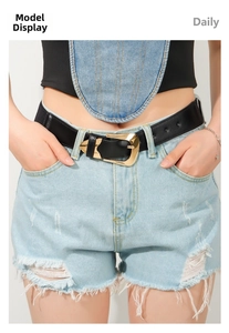 Detail of a black leather belt with a decorative gold geometric buckle on blue jeans
