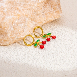Detailed close-up of gold hoop earrings with red enamel cherry pendants and green leaves