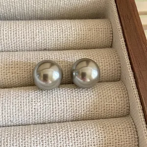 Close-up of minimalist dark silver pearl stud earrings on linen jewelry tray