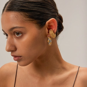 Detail of 18k gold hammered C-shaped ear cuff and bicolor flower hoop earrings on model