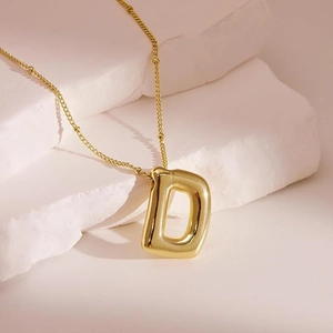 Macro shot of 18K gold balloon letter D pendant necklace on a white stone background