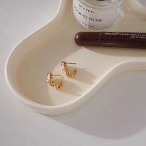 Detailed close-up of golden wavy stud earrings with round zircons on a white tray