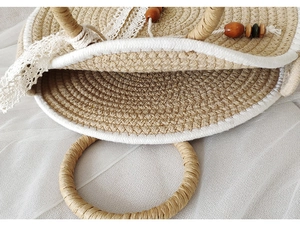 Close-up of woven straw bag showing white lace trim, wooden beads, and natural texture