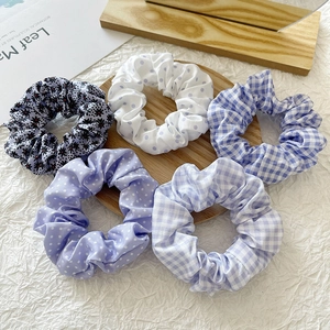 Detail view of five floral and polka dot fabric scrunchies on a wooden tray background