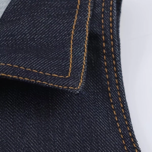 Detailed close-up of dark blue denim fabric with reinforced orange double stitching seams