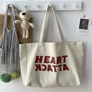 Close-up of cream canvas tote bag with red Heart Attack lettering on a wall hook