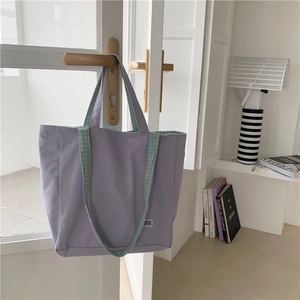 Detalle del bolso de lona lavanda con asas de cuadros verdes colgado en una puerta