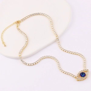 Golden evil eye necklace with blue gemstone and clear cubic zirconia on white background