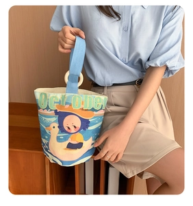 Detail of canvas bucket bag featuring cartoon illustration and blue ribbon handle