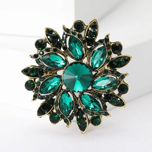 Macro detail of vintage floral brooch with emerald green crystals and antique gold finish