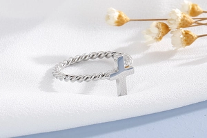 Macro detail of twisted rope band and silver cross ring on elegant textured fabric