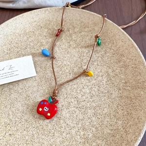 Détail d'un pendentif pomme rouge créatif avec des perles colorées sur un collier tressé