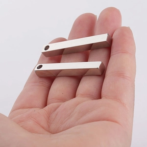 Detailed view of two mirror-polished silver rectangular pendants held in a hand