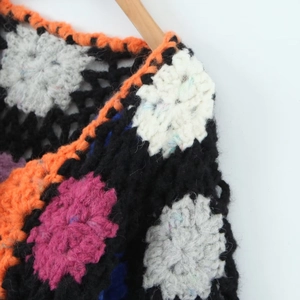 Close-up of handmade crochet cardigan featuring colorful floral knit patterns on black yarn