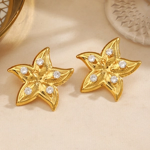 Golden starfish earrings with clear round zircons on elegant beige fabric background