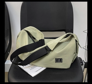 Light green large capacity sports bag with adjustable black shoulder strap on black chair