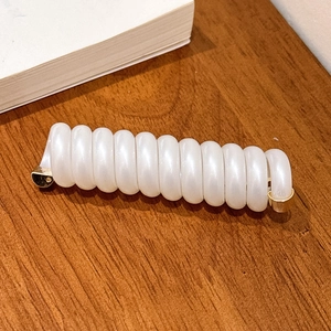 Détail d'un élastique spirale blanc nacré avec embouts dorés sur une surface en bois