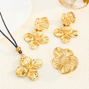 Détail à plat de parure collier, boucles d'oreilles et broche fleur dorée sur tissu