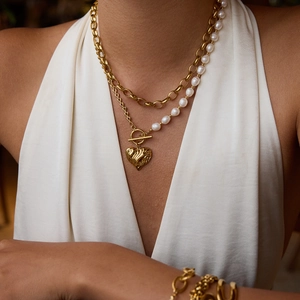 Detail of layered gold link chain and freshwater pearl necklace with heart pendant