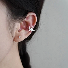 Close-up of a silver swallow-shaped ear cuff and stud earring on a female model