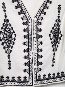 Detail view of ethnic embroidery patterns and fabric buttons on white cotton linen vest