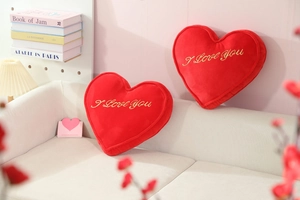 Close-up of red heart plush pillows with gold I Love You embroidery on a cozy sofa