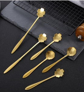 Detail of six golden stainless steel flower spoons with cherry blossom patterns on dark slate