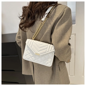 White quilted crossbody bag with gold chain strap shown on model from side view