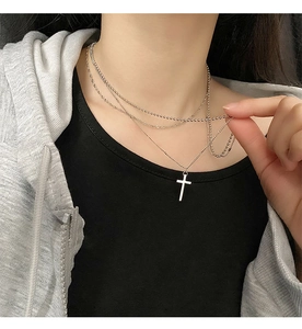 Close-up of a layered stainless steel necklace with a silver cross pendant on a model