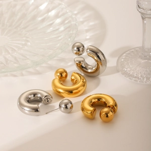 Macro detail of polished gold and silver C-shaped sphere stud earrings on a beige surface