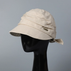Detail of beige cotton linen sun hat with pleated texture and gold metal logo plaque