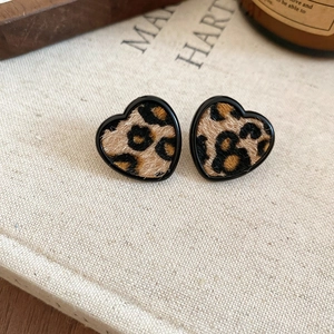 Detail of heart-shaped leopard print earrings with flocking texture on a linen book