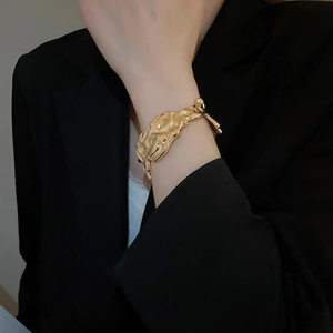 Close-up of golden irregular wrinkled open bangle with metallic hammered texture on wrist