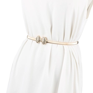 Vue détaillée d'une ceinture élastique dorée avec nœud en strass sur une robe blanche