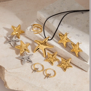 Flat lay of star-shaped stainless steel necklace and rings on textured beige stones