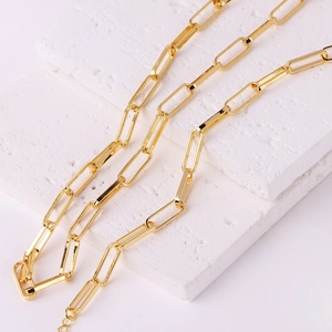 Chic gold paperclip link necklace displayed on white stone blocks in a minimalist aesthetic