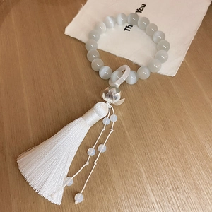 Macro detail of cat eye stone beads with silver lotus flower and silky white tassel