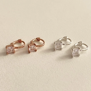 Macro detail of silver and rose gold square zircon hoop earrings on a beige surface